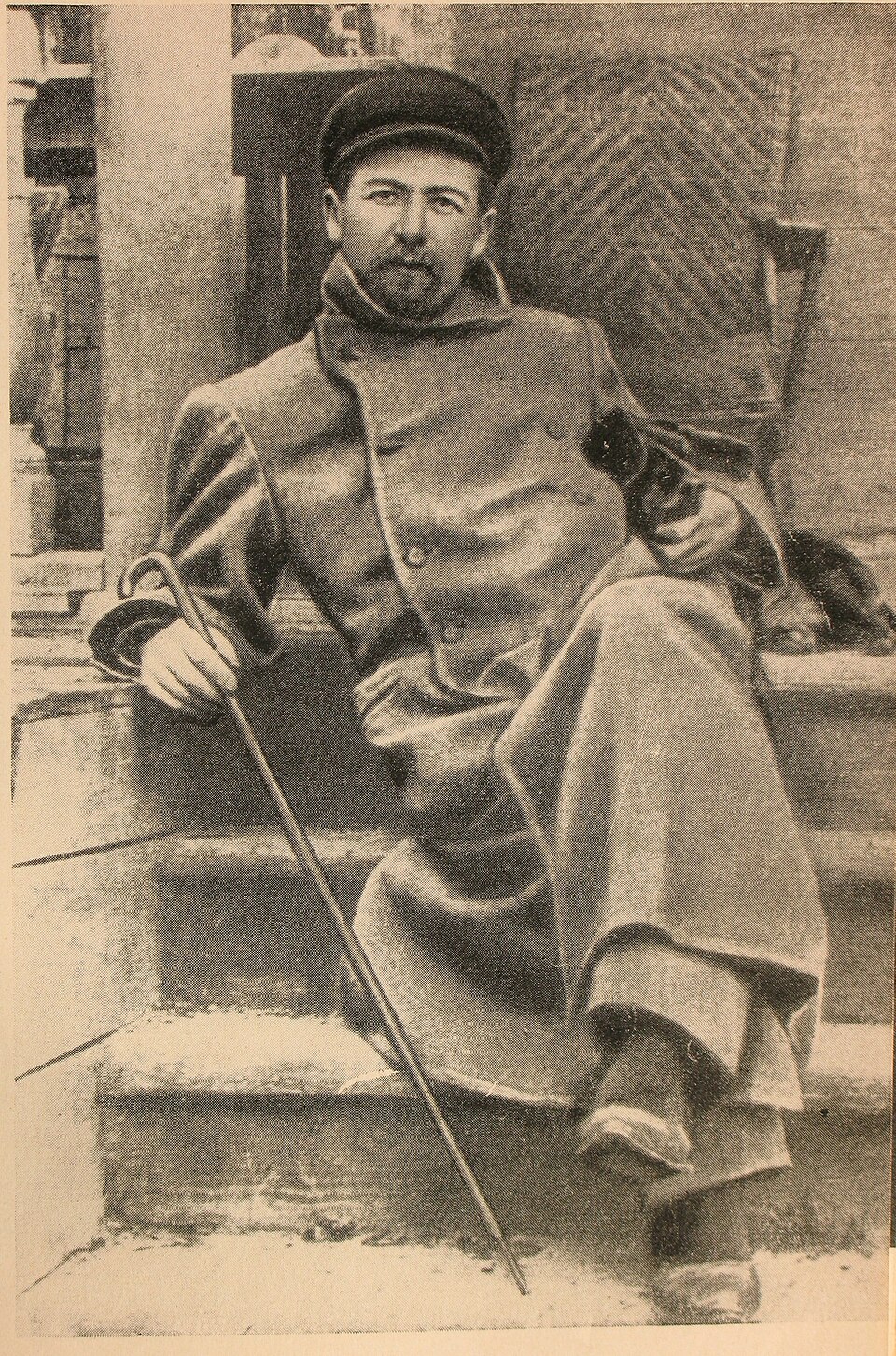 Photograph. Chekhov reclines on steps with cane and dachsund.